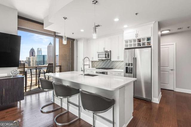 kitchen with dark wood finished floors, an island with sink, a sink, appliances with stainless steel finishes, and tasteful backsplash