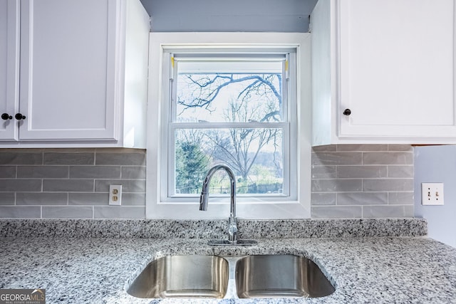 kitchen featuring a wealth of natural light, white cabinets, backsplash, and a sink