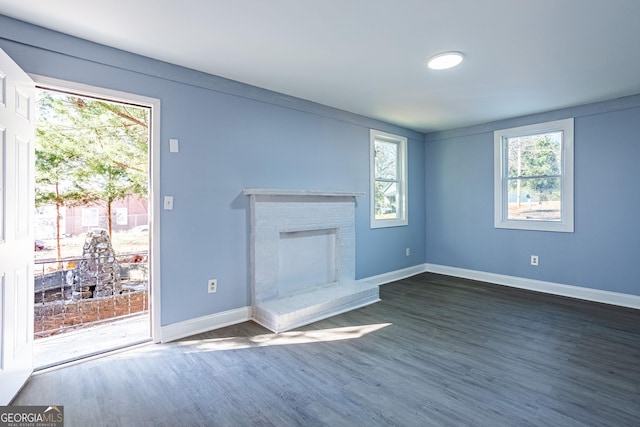 unfurnished living room featuring baseboards, a brick fireplace, and dark wood finished floors