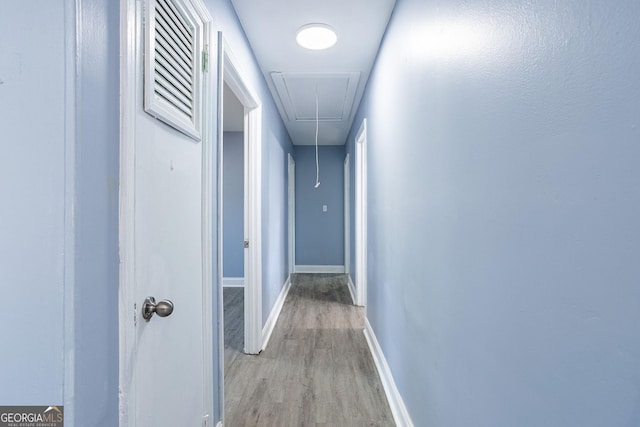 corridor featuring visible vents, baseboards, attic access, and light wood finished floors