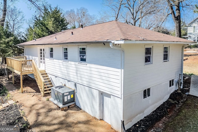 rear view of house with a deck, stairway, central AC unit, and roof with shingles