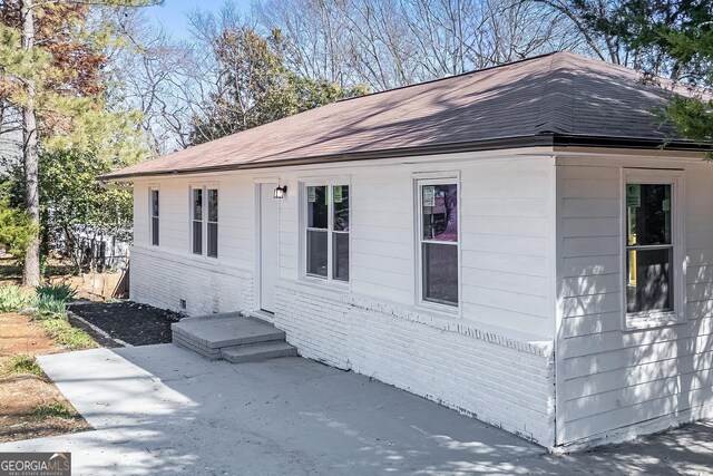 view of property exterior with brick siding and roof with shingles