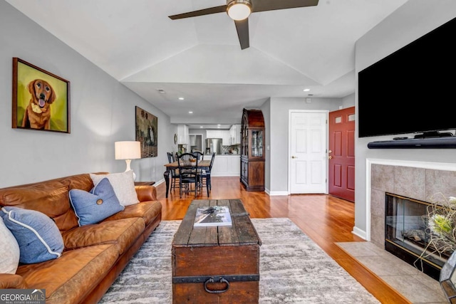 living area featuring baseboards, wood finished floors, a tile fireplace, and vaulted ceiling