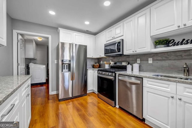 kitchen with light wood-style flooring, a sink, tasteful backsplash, white cabinetry, and stainless steel appliances