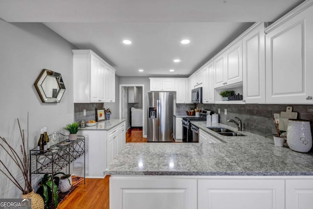 kitchen featuring light stone counters, a peninsula, stainless steel appliances, white cabinetry, and a sink