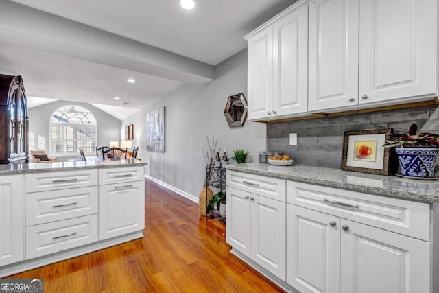 kitchen with backsplash, lofted ceiling, recessed lighting, wood finished floors, and white cabinetry