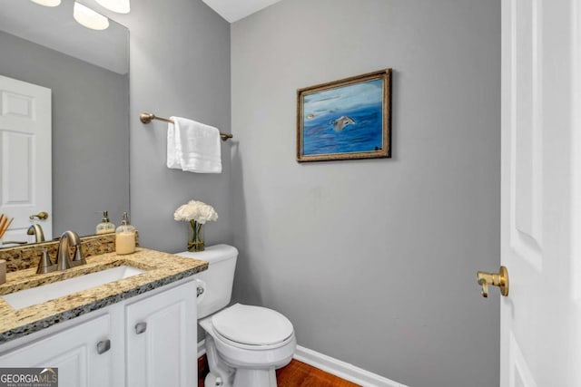 half bath with toilet, vanity, baseboards, and wood finished floors