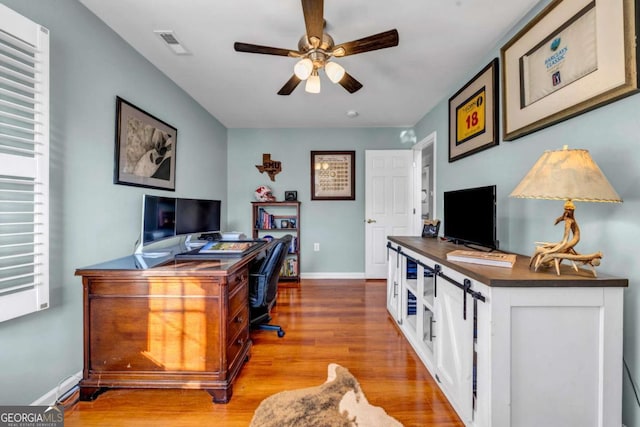 home office with a ceiling fan, wood finished floors, visible vents, and baseboards