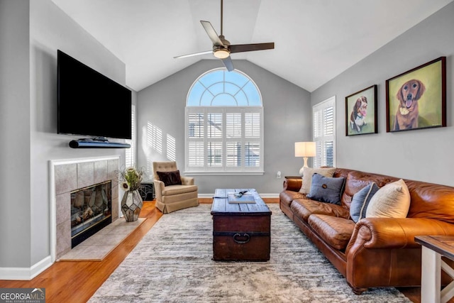 living area with wood finished floors, baseboards, lofted ceiling, a fireplace, and ceiling fan