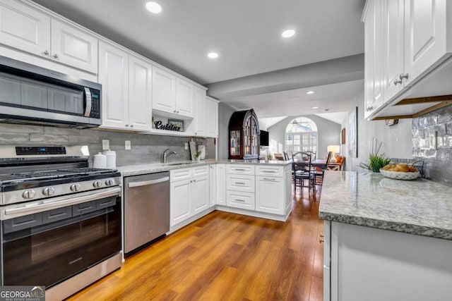 kitchen featuring light stone countertops, a peninsula, stainless steel appliances, wood finished floors, and white cabinetry