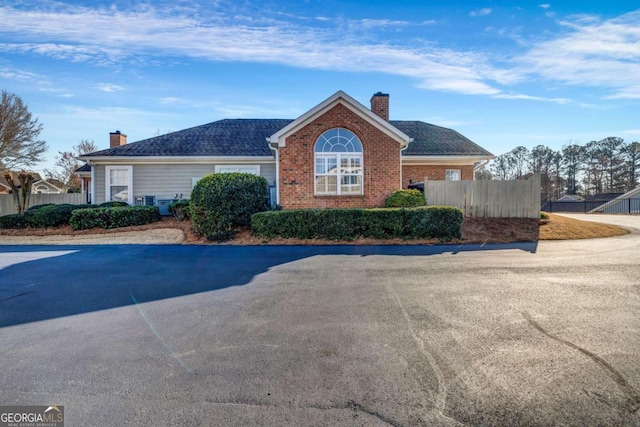 view of front of home featuring brick siding, a chimney, and fence