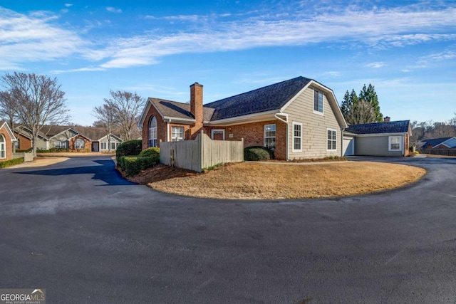 view of home's exterior featuring fence, a chimney, a garage, aphalt driveway, and brick siding