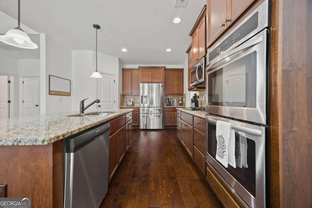 kitchen featuring light stone countertops, dark wood finished floors, brown cabinets, appliances with stainless steel finishes, and a sink