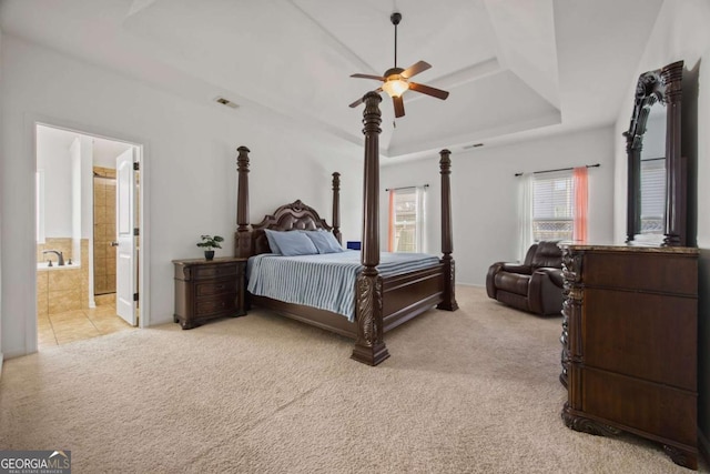 bedroom featuring visible vents, ceiling fan, light colored carpet, ensuite bathroom, and a raised ceiling