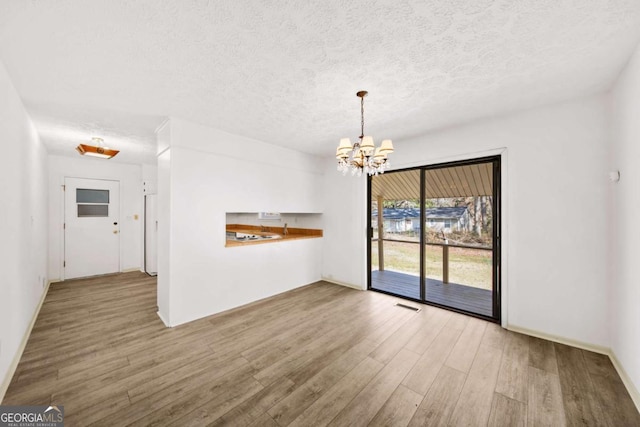 unfurnished dining area with a notable chandelier, wood finished floors, visible vents, and a textured ceiling