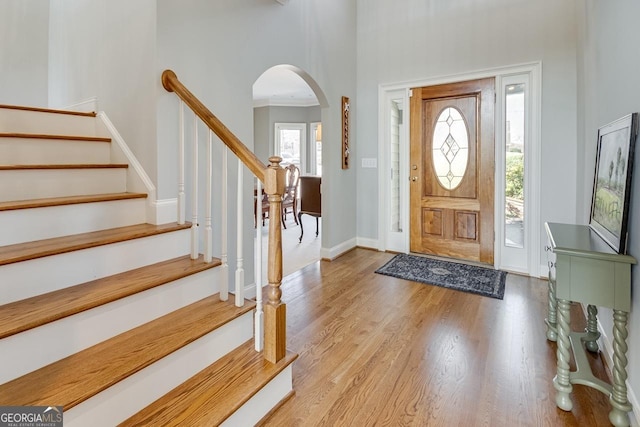 entrance foyer with stairway, wood finished floors, baseboards, a high ceiling, and arched walkways