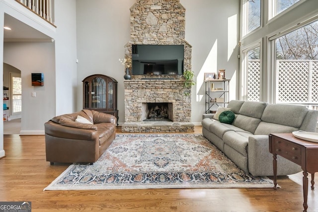 living area with wood finished floors, arched walkways, a high ceiling, a fireplace, and baseboards