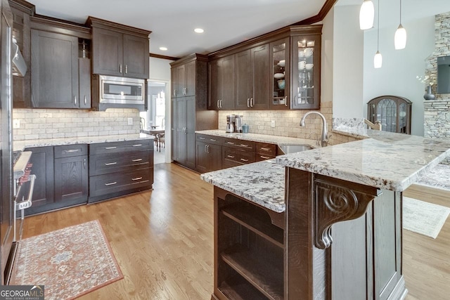 kitchen featuring stainless steel microwave, dark brown cabinets, light wood finished floors, and a sink