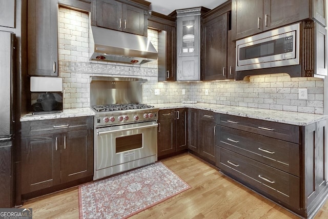 kitchen featuring under cabinet range hood, dark brown cabinets, stainless steel appliances, and light wood-type flooring