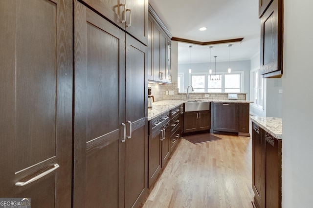 kitchen featuring light stone countertops, a peninsula, a sink, decorative backsplash, and light wood-style floors