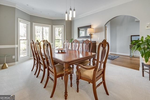 dining space featuring light colored carpet, crown molding, baseboards, and arched walkways