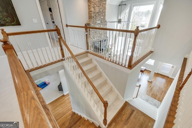 stairway with ceiling fan, a high ceiling, and wood finished floors