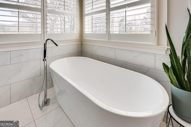 full bathroom featuring tile walls, a soaking tub, a healthy amount of sunlight, and marble finish floor