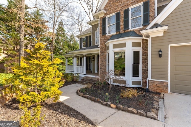 property entrance featuring stone siding, a porch, and a garage