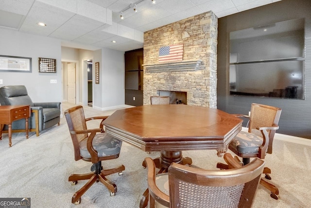 home office with a stone fireplace, rail lighting, baseboards, and light carpet