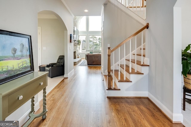 foyer entrance featuring ornamental molding, wood finished floors, arched walkways, baseboards, and stairs