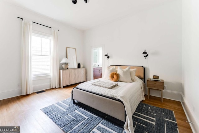 bedroom featuring visible vents, radiator heating unit, baseboards, and wood finished floors