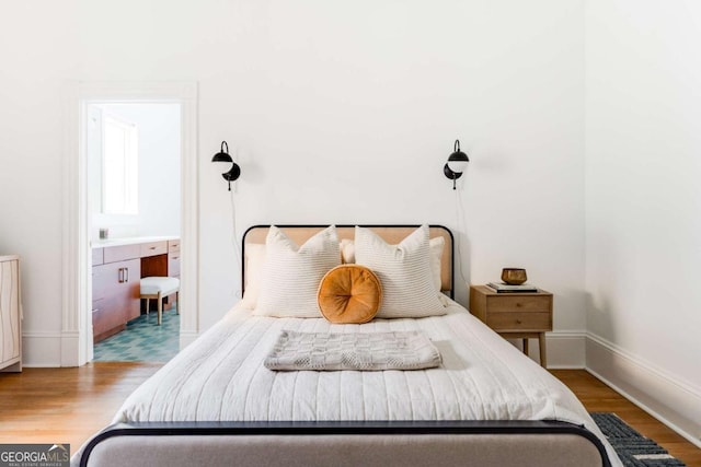 bedroom with connected bathroom, baseboards, and wood finished floors