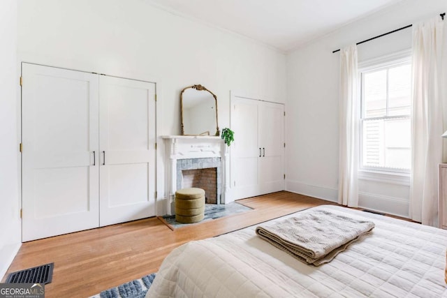 bedroom featuring visible vents, baseboards, multiple closets, a tile fireplace, and wood finished floors