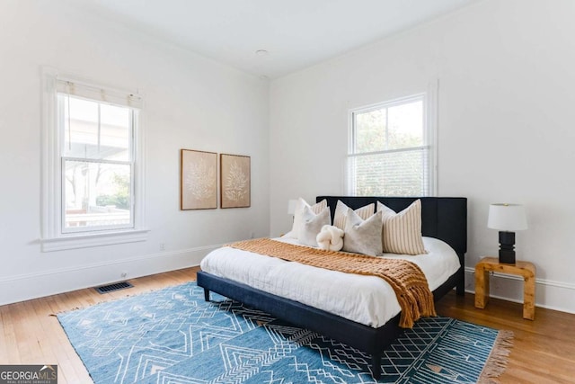 bedroom with multiple windows, wood finished floors, visible vents, and baseboards