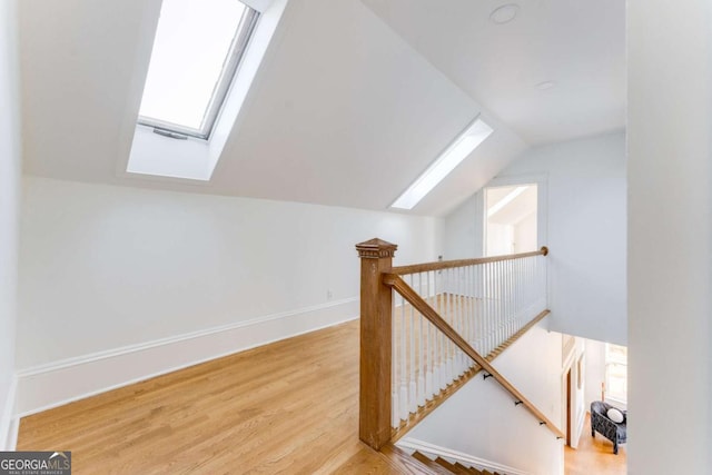 bonus room featuring baseboards, vaulted ceiling with skylight, and wood finished floors