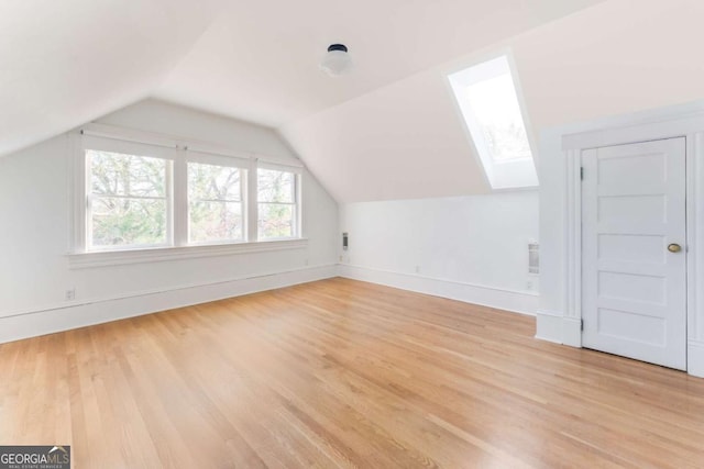 additional living space featuring vaulted ceiling with skylight, light wood-style floors, and baseboards