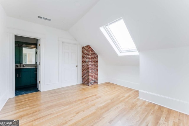 bonus room with visible vents, a sink, wood finished floors, vaulted ceiling with skylight, and baseboards