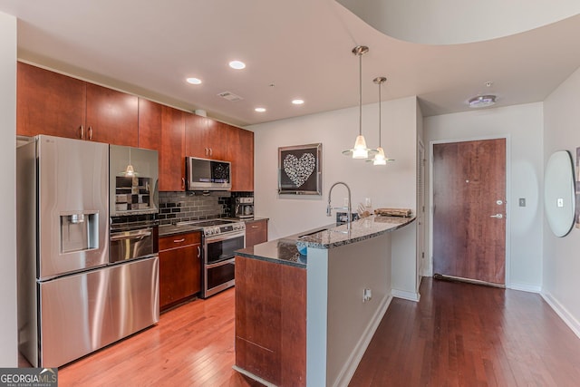 kitchen with a peninsula, a sink, hardwood / wood-style flooring, appliances with stainless steel finishes, and tasteful backsplash