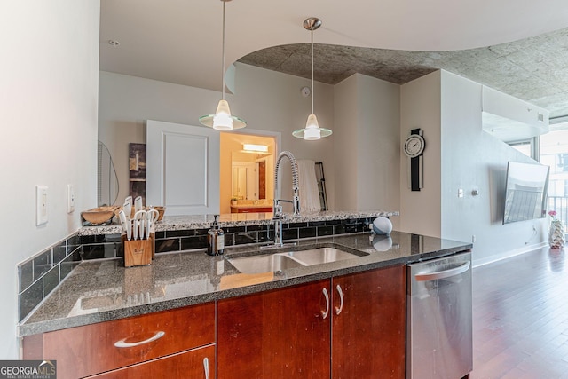 kitchen with a sink, dark stone countertops, stainless steel dishwasher, wood finished floors, and hanging light fixtures