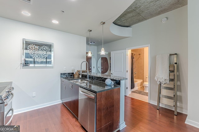 kitchen with a sink, dark wood finished floors, dark stone counters, appliances with stainless steel finishes, and a peninsula