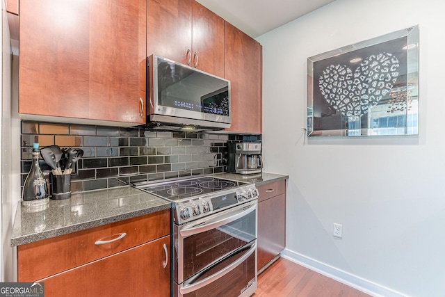 kitchen featuring dark stone countertops, baseboards, stainless steel appliances, light wood-style floors, and backsplash