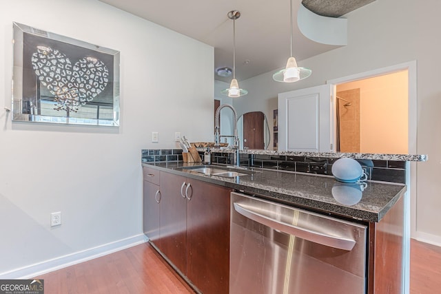 kitchen with dark stone counters, a peninsula, stainless steel dishwasher, light wood-style floors, and a sink