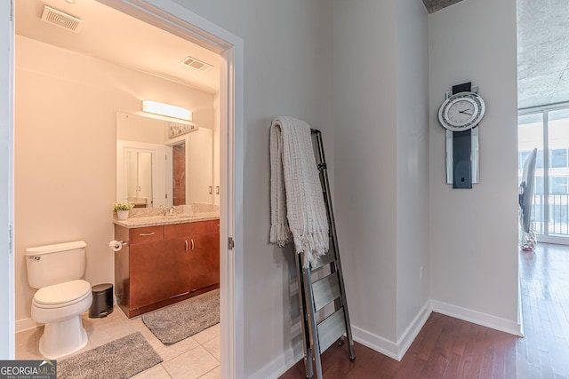 half bath with visible vents, toilet, wood finished floors, baseboards, and vanity