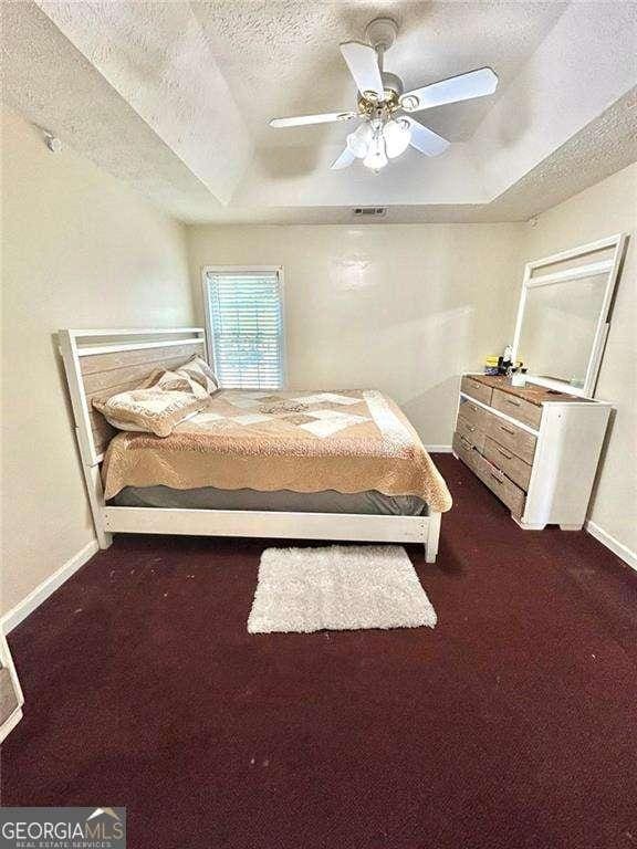 3672 Misty Oak Dr, Flowery Branch, GA 30542 - bedroom with a raised ceiling, a textured ceiling, dark colored carpet, and a ceiling fan