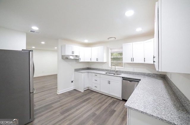 kitchen featuring wood finished floors, a sink, white cabinets, under cabinet range hood, and appliances with stainless steel finishes