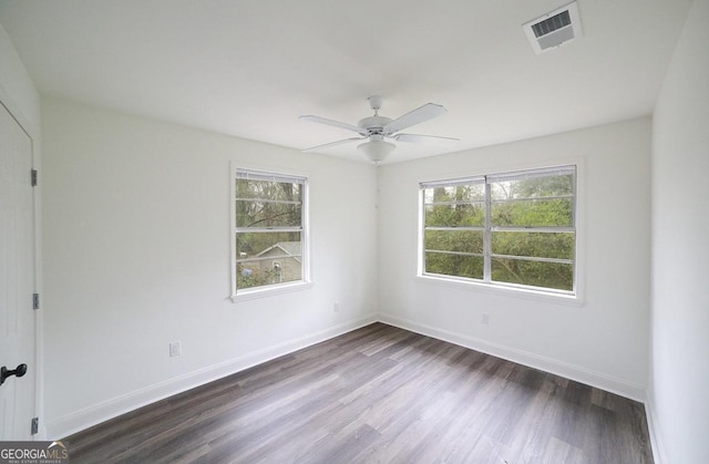 empty room featuring visible vents, plenty of natural light, baseboards, and dark wood-style flooring