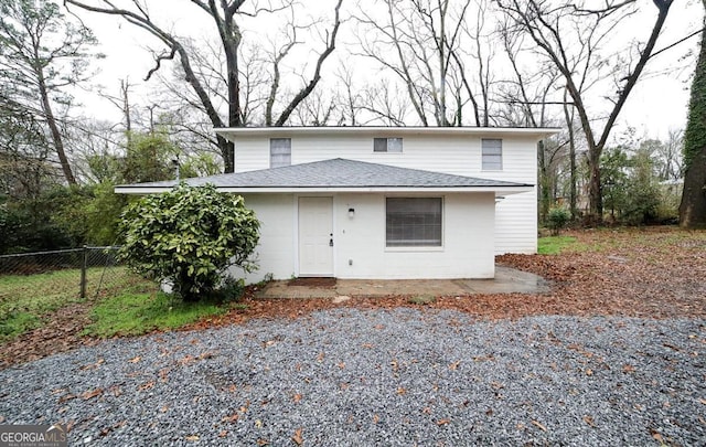 traditional home featuring a patio, fence, and roof with shingles