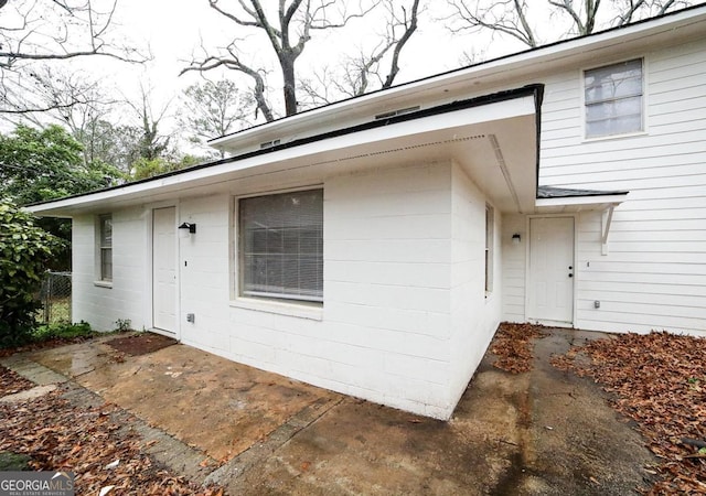 doorway to property featuring concrete block siding, a patio, and fence