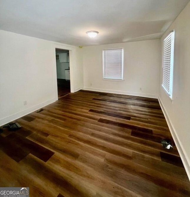 spare room featuring baseboards and dark wood-style flooring