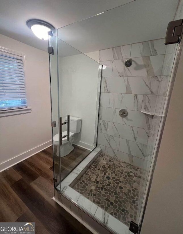 bathroom featuring a stall shower, toilet, baseboards, and wood finished floors